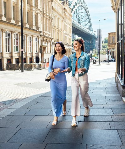 Two smiling women walking down a quiet street on a sunny day. 